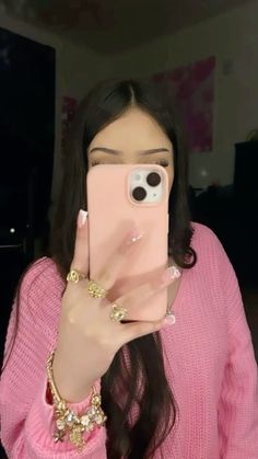 a woman taking a selfie with her cell phone in front of her face and wearing a pink sweater