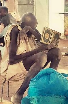 a man sitting on top of a chair next to a blue bag and another person holding an open book