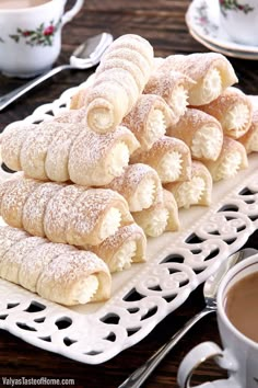 a white plate topped with powdered sugar covered pastries next to a cup of coffee