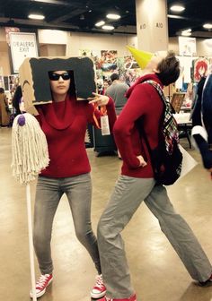 two women in red sweaters and grey pants carrying cardboard boxes on their heads while walking through a store