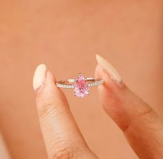 a woman's hand holding a ring with a pink stone in it and diamond band