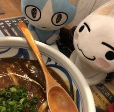 a bowl of soup with a cat stuffed animal next to it on a wooden table