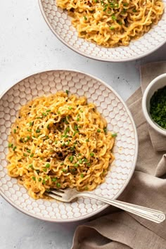 two white plates filled with pasta on top of a table next to a bowl of parsley