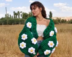 a woman standing in a field wearing a green knitted sweater with white flowers on it