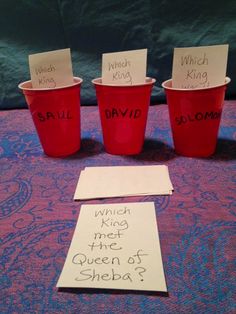 three red cups sitting on top of a table with notes written on them and paper attached to the cups