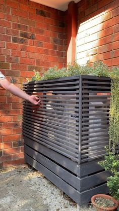 a man standing next to a planter in front of a brick building with plants growing out of it