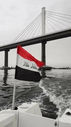 a flag is flying on the back of a boat in front of a large bridge