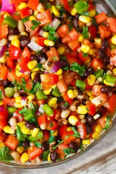 a glass bowl filled with corn, black beans, and cilantro peppers on top of a wooden table