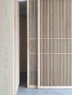 an open wooden door with vertical slats on the outside and inside, in front of a white wall