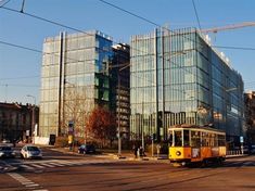 a yellow trolley driving down a city street next to tall buildings with glass windows on each side