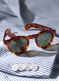 a pair of sunglasses sitting on top of a striped shirt next to two white buttons