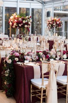 the tables are set with white and burgundy linens, gold chairs, and floral centerpieces