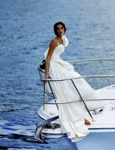 a woman in a white dress standing on the back of a boat