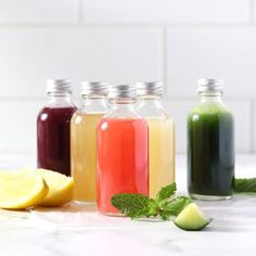 four bottles filled with liquid next to sliced lemons and mint on a white counter