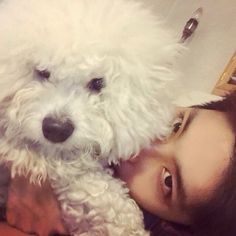 a woman is holding a white dog in her arms while she looks at the camera