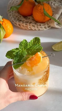 a hand holding a glass with oranges and mint garnish on it next to some fruit