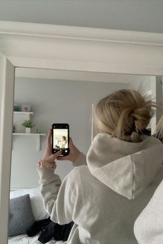 a woman taking a selfie in front of a mirror with her cell phone while sitting on a bed