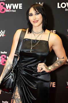 a woman in a black dress with tattoos on her arm and shoulder, posing for the camera