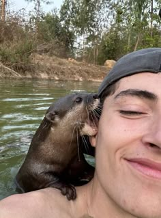 a man is holding an otter up to his face in the water while he smiles