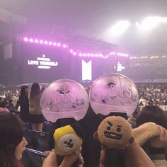 two people holding up stuffed animals in front of a crowd at a concert with purple lights