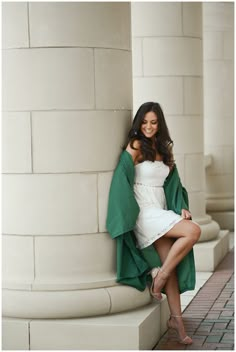 a beautiful woman leaning against a pillar wearing a green jacket and white dress with high heels