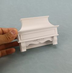 a hand is holding a miniature white bed