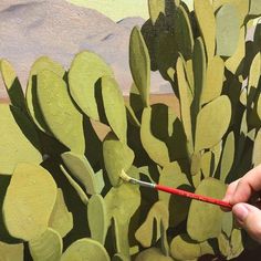 a person is painting a cactus on the wall with green paint and a red brush