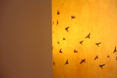 birds are flying in the sky on a yellow lamp shade hanging from a white wall