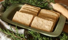 four squares of shortbread on a green plate next to a spatula and some greenery