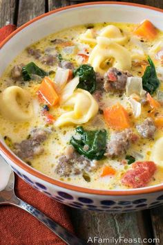 a bowl of pasta soup with meat, cheese and spinach in it on a wooden table