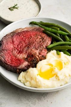 steak, mashed potatoes and green beans on a white plate with ranch dressing in the background