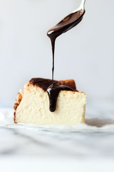 a piece of cheesecake with chocolate sauce being drizzled on top