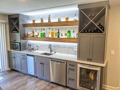 an empty kitchen with stainless steel appliances and bottles on the wall behind it, along with shelves that hold liquor