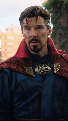 the doctor strange looking man is wearing a red cape and blue shirt with gold accents