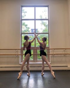 two ballerinas standing in front of a window with their hands on each other