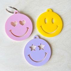 three smiley face shaped key chains on a white surface with one yellow and one pink