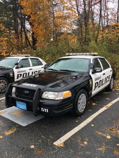 two police cars parked next to each other in a parking lot with fallen leaves on the ground