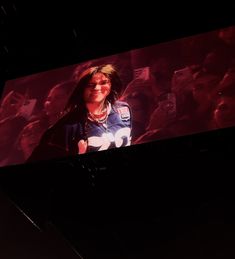 a woman standing in front of a large screen with people on it's sides