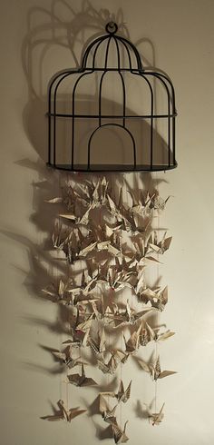 a birdcage hanging on the wall with origami birds in it