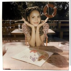 a woman sitting at a table with her hands on her face and holding up the peace sign