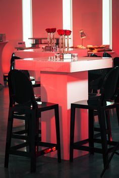 two black chairs sitting at a white table with red lights on the wall behind it