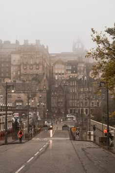 an empty city street in the rain with buildings on both sides and people walking down the road