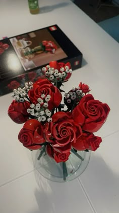 a vase filled with red roses sitting on top of a table next to a box