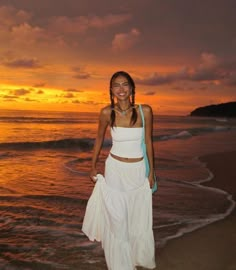 a woman standing on top of a sandy beach next to the ocean at sunset or dawn