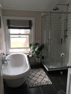 a white bathtub sitting next to a window in a bathroom on top of a black and white rug