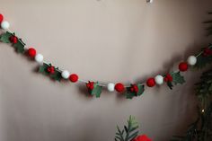 a christmas garland with holly leaves and pom - poms hanging on a wall