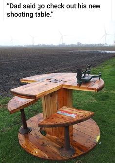 a wooden table sitting in the middle of a field with wind turbines behind it and an advertisement on top