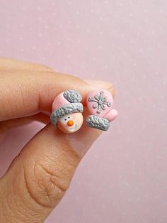 a hand holding a tiny snowman ring on it's fingers with pink and gray decorations