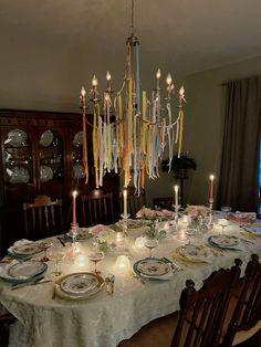 a dining room table is set with plates and place settings, candles in the middle