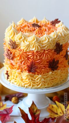 a cake with orange and yellow frosting decorated with autumn leaves on a white pedestal